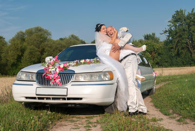 Couple by car on field against sky