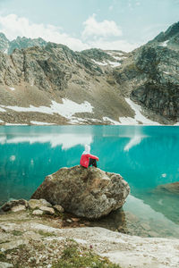 Man on rock by lake against mountains