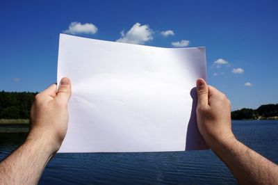 Close-up of hand holding paper against blue sky