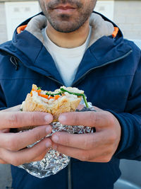 Midsection of man wearing hooded jacket holding sandwich