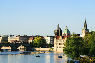 Bridge over river by buildings in city against clear sky