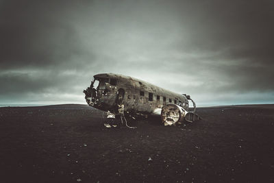 Abandoned airplane on sand at beach against sky