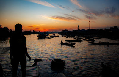 Rear view of silhouette man standing by lake during sunset