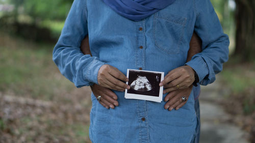 Midsection of pregnant woman holding transfer prints with husband hands on belly
