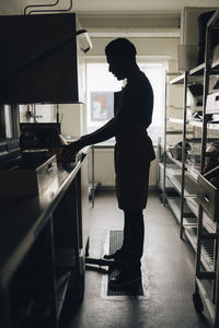 Full length of male baker washing dishes while standing in commercial kitchen