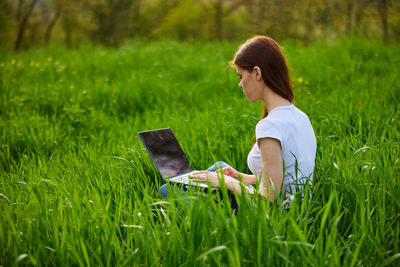 Young woman using laptop while sitting on field