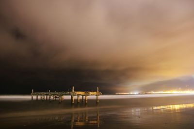 Damaged pier against cloudy sky at beach during night