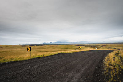 Road passing through field against sky