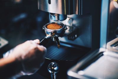 Cropped hand of person holding portafilter with ground coffee in cafe