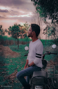 Side view of young man sitting on field against sky