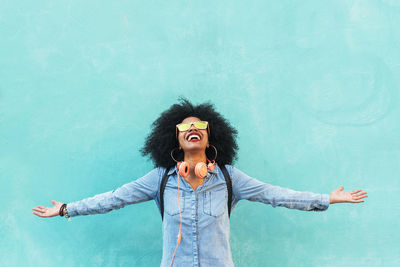 Happy young woman with arms outstretched standing against blue wall