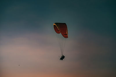 Low angle view of silhouette people paragliding against sky during sunset