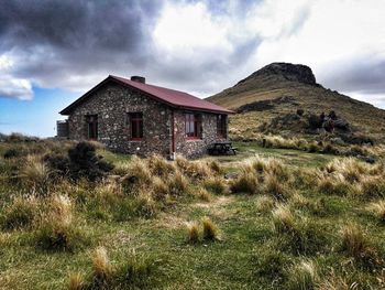 Old stone hut in a field by a mountain.