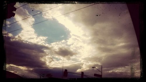 Low angle view of power lines against cloudy sky