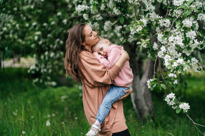 Young mother with her daughter in her arms in a blooming apple orchard