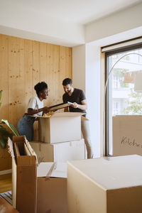 Multiracial couple removing frame from cardboard box while standing at new home