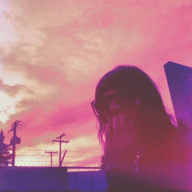 sky, low angle view, lifestyles, silhouette, leisure activity, cloud - sky, sunset, built structure, architecture, building exterior, dusk, standing, outdoors, waist up, cloud, three quarter length, technology, headshot