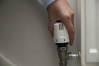 Hand of girl adjusting radiator thermostat regulator at home