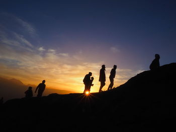 Silhouette people standing on land against sky during sunset