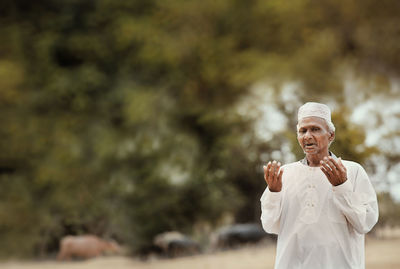 Portrait of senior man gesturing while standing outdoors