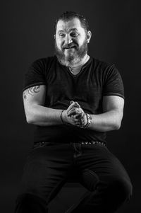 Portrait of smiling man sitting against black background