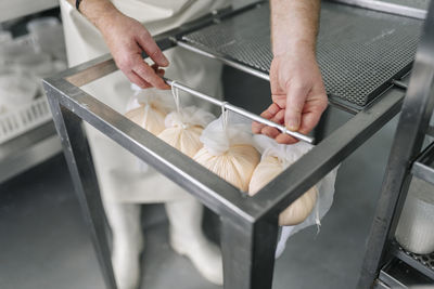 Chef holding rod of hanging cheese wrapped in clothes at factory