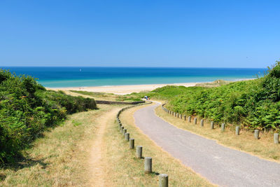 Road by sea against clear blue sky