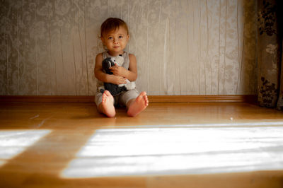 Cute boy with soft toy sitting in front of wall at home