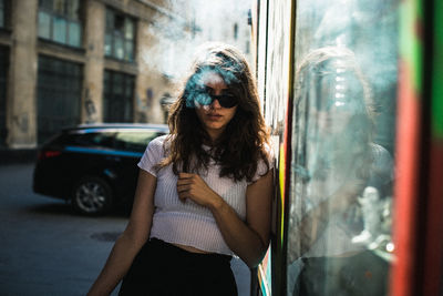 Young woman wearing sunglasses standing by car in city