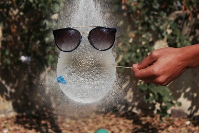 Cropped hand bursting water balloon with sunglasses