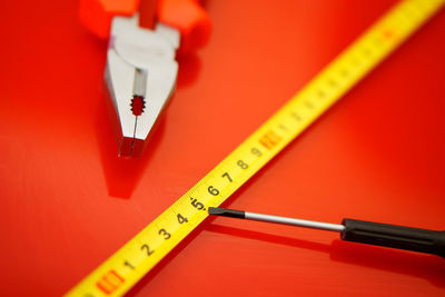 Close-up of screwdriver and pliers by measuring tape over red background
