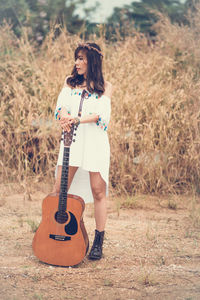 Full length of young woman holding guitar on field
