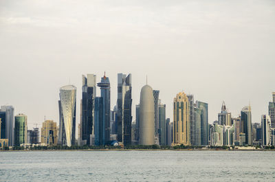 Sea by modern buildings against sky in city