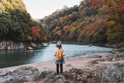 Rear view of woman standing on rock by lake