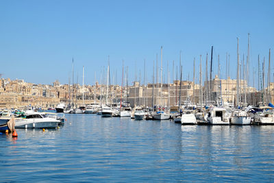 Sailboats moored on harbor against clear blue sky