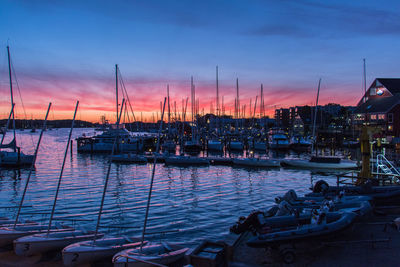 Sailboats moored in harbor at sunset