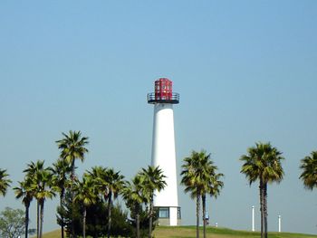 View of lighthouse and palm trees against blue sky