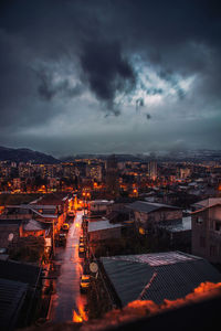 Illuminated cityscape against cloudy sky at dusk