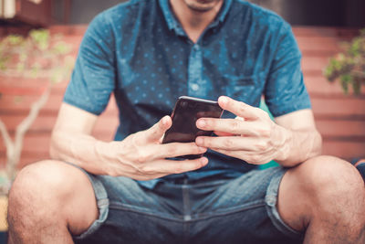 Midsection of man using mobile phone while sitting outdoors