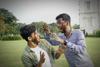 Male friends with cake on face standing at lawn