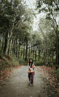 Woman standing on footpath amidst trees in forest