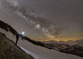 Man with flashlight standing against star field on snowcapped mountain