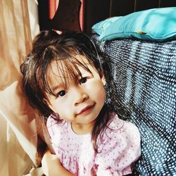 Portrait of cute girl sitting by bed at home