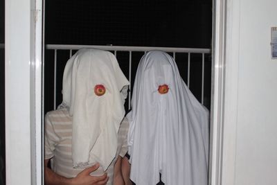 Male friends faces covered with white fabrics in balcony at night