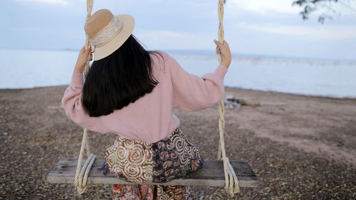 Rear view of woman standing on swing at beach