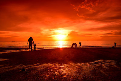 Silhouette people standing on beach against orange sky