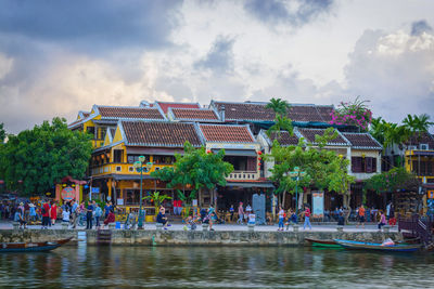 People on lake by buildings against sky