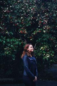 Young woman looking away while standing against tree