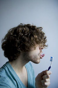 Close-up of young man sticking out tongue while holding toothbrush against wall