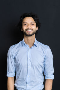 Portrait of smiling young man against black background